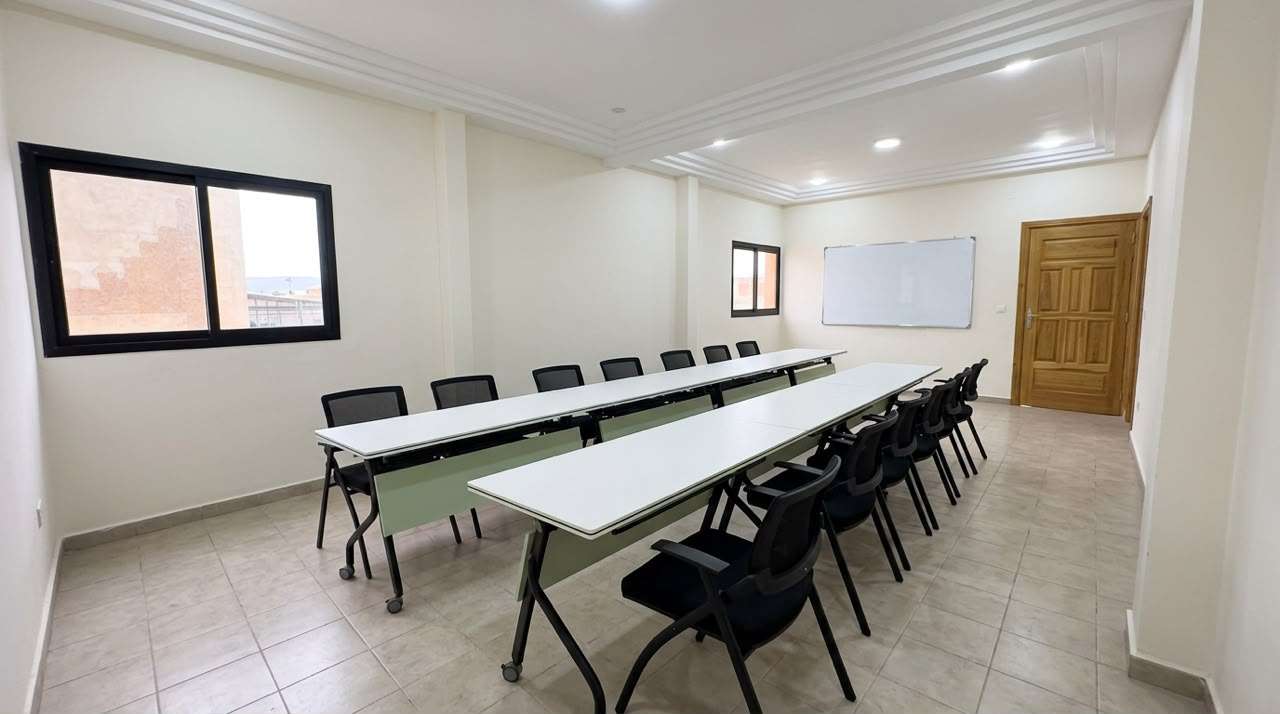 Salle de formation du centre, longues tables de travail alignées en enfilade devant les fenêtres.